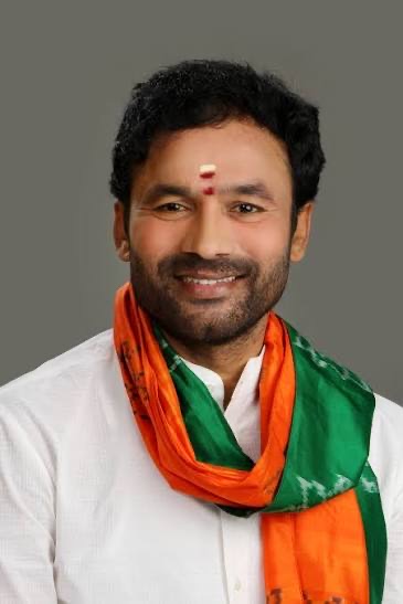 Earlier portrait of G. Kishan Reddy smiling, in a white kurta with a saffron and green stole, against a grey background