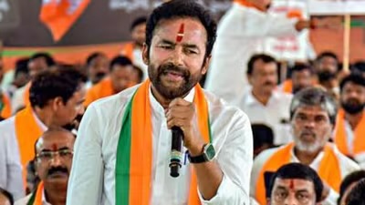 G. Kishan Reddy in a saffron and green stole speaking into a microphone while seated among party workers