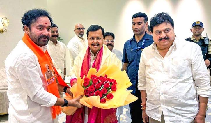 G. Kishan Reddy in a saffron stole greeting a colleague who holds a large bouquet of red roses, with others standing around them