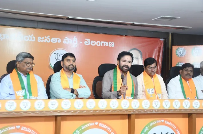 G. Kishan Reddy speaking at a press conference table with party colleagues in saffron and green stoles, under a BJP Telangana banner