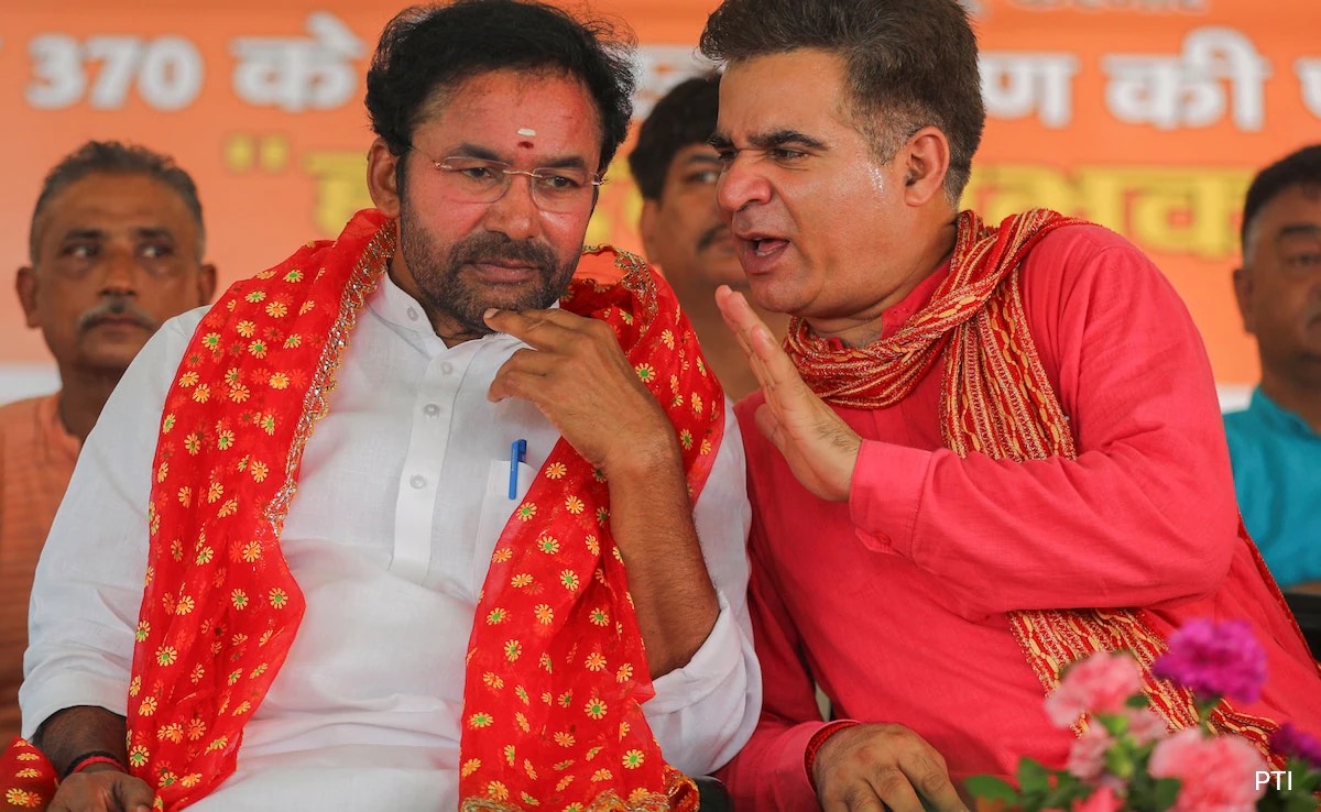 G. Kishan Reddy in a red and gold stole listening as Ravinder Raina, at the time Jammu and Kashmir BJP president, speaks to him on stage at a public event