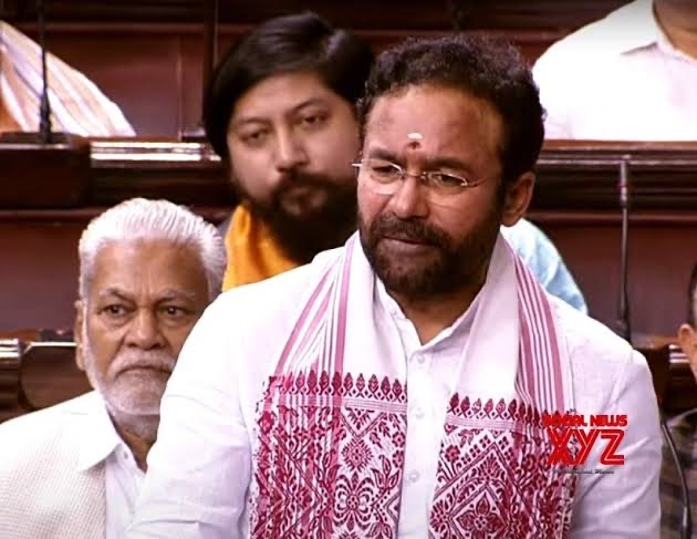 G. Kishan Reddy in a white kurta and a white stole with red woven motifs, standing to speak in Parliament, members seated behind him
